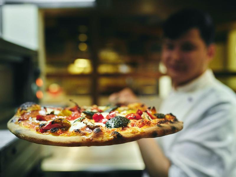 Mann hält frisch gebackene Pizza mit verschiedenen Belägen in einer Küche.