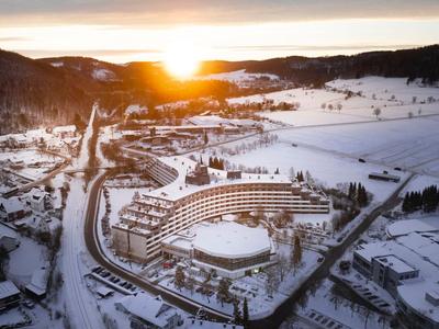Besneeuwd winterlandschap met een groot hotel en zonsopgang op de achtergrond.