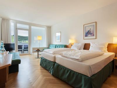 Lichte hotelkamer met tweepersoonsbed, bureau en balkon met uitzicht op de bergen.