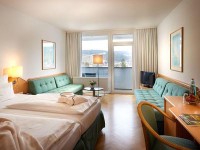 Hotelkamer met twee bedden, twee groene banken, bureau en balkon met uitzicht.