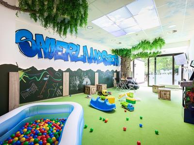 Lichte kinderkamer met tapijt, ballenbak, kleurrijk speelgoed en muurschildering.