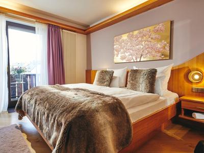 Gemütliches Hotelzimmer mit großem Bett, braunem Fellüberwurf und Zugang zu Balkon.