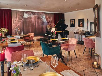 Eleganter Hotelrestaurant mit bunten Sesseln, Tischen und einem schwarzen Flügel in warmem Licht.