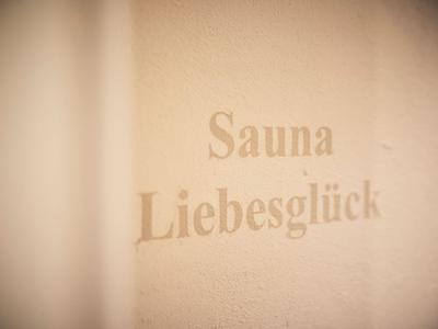 Verwischter Schriftzug 'Sauna Liebesglück' an einer beige Wand.