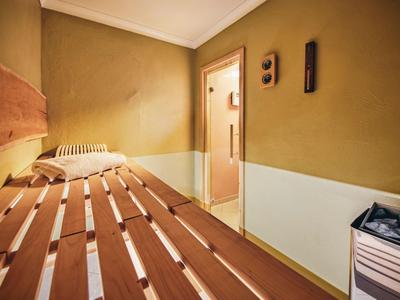 Saunaraum mit Holzbänken, gelben Wänden und einem kleinen Heizgerät.