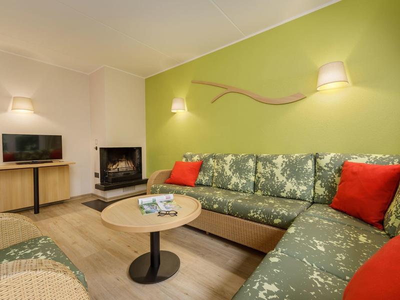 Gemütliches Wohnzimmer mit grünem Sofa, roten Kissen, Kamin, kleinem Fernseher und rundem Holztisch.