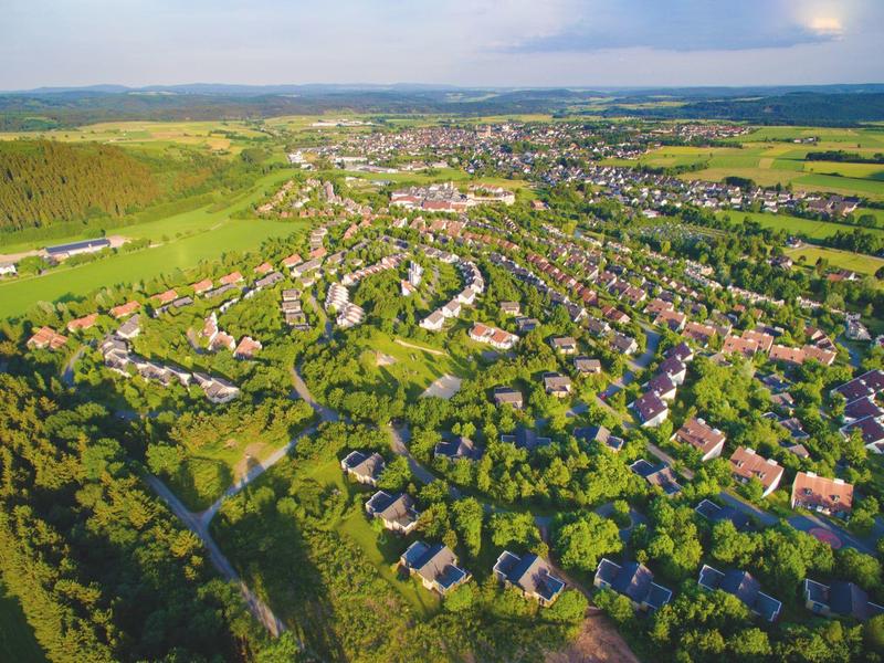 Luftaufnahme einer weitläufigen Wohnsiedlung mit vielen Häusern, Grünflächen und Feldern im Hintergrund.