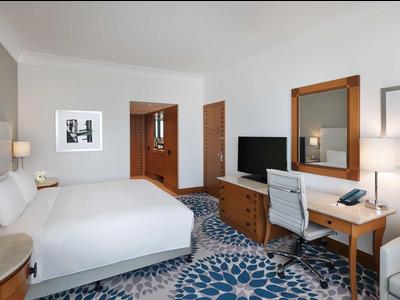 Modernes Hotelzimmer mit großem Bett, blau gemustertem Teppich und Holzmöbeln.