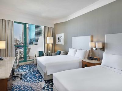 Modernes Hotelzimmer mit zwei Doppelbetten, grauen Wänden und großem Fenster mit Stadtblick.