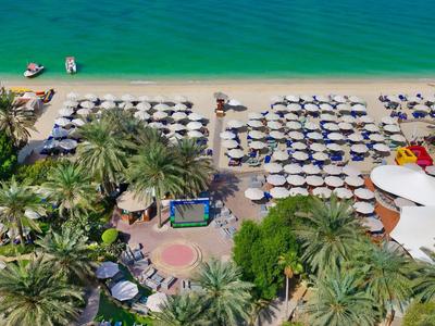 Strand mit türkisfarbenem Wasser, Palmen, vielen Sonnenschirmen und Strandliegen in Reihen.
