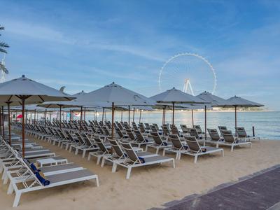 Strand mit Liegestühlen und Sonnenschirmen am Meer unter blauem Himmel.
