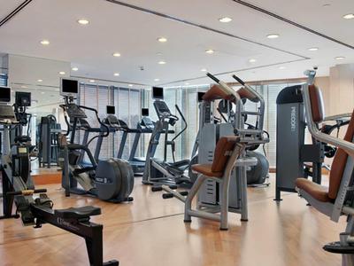Moderner Fitnessraum mit Cardio- und Kraftgeräten, hellem Holzfußboden und großen Fenstern.
