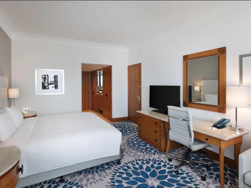 Modernes Hotelzimmer mit großem Bett, blau gemustertem Teppich und Holzmöbeln.