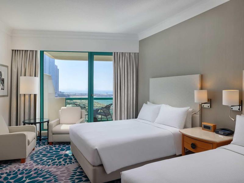 Helles Hotelzimmer mit zwei Betten, großen Fenstern, Teppichboden und moderner Einrichtung.