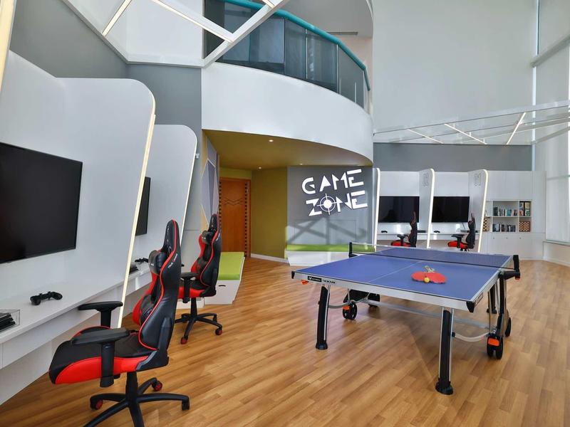 Moderner Aufenthaltsraum mit Tischtennisplatte, Gaming-Stühlen, TV und hellen, geschwungenen Wänden.