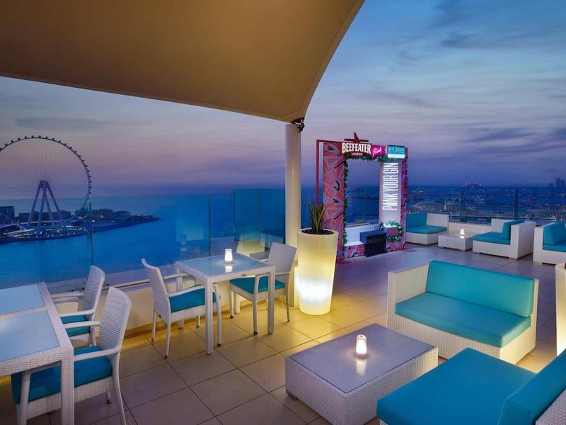 Dachterrasse mit moderner Sitzmöbeln, Beleuchtung und Blick aufs Meer bei Abenddämmerung.