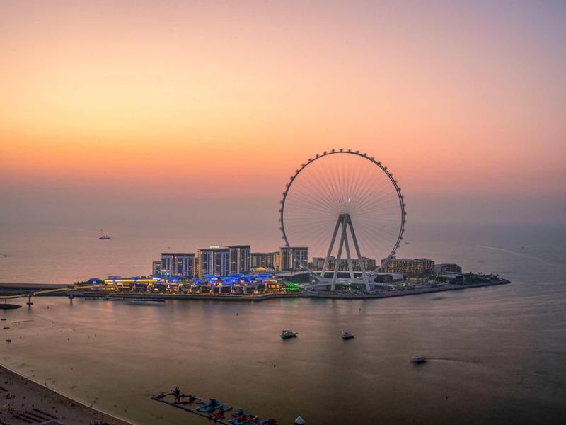 Küsteninsel mit großem Riesenrad, Gebäuden und ruhigem Meer bei Sonnenuntergang.