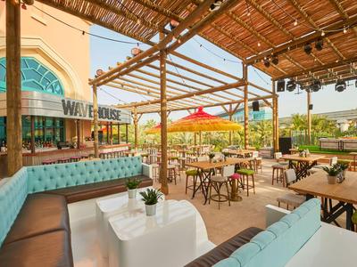 Area esterna aperta con tavoli sotto un pergolato in legno accanto a un edificio.