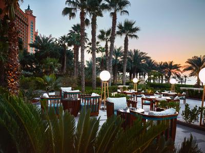 Ristorante all'aperto con tavoli e sedie circondati da palme al tramonto.
