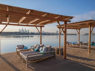 Area salotto con pergolati in legno con vista su acqua e skyline della città sotto un cielo sereno.