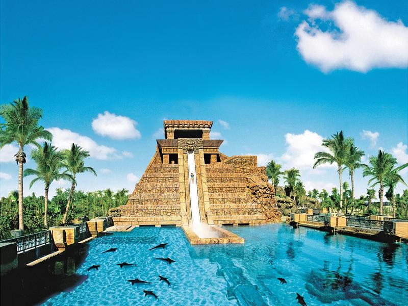 Großer Wasserpark mit Pyramidenrutsche, blauem Pool und Palmen vor klarem Himmel.