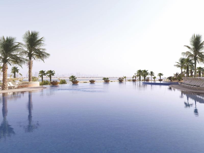 Großer, ruhiger Pool mit Palmen am Rand unter klarem, hellem Himmel.