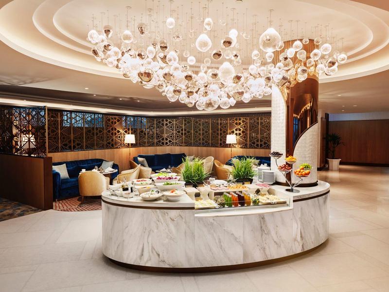 Elegantes Buffet mit Marmorinsel, dekorativen Speisen und moderner Beleuchtung in hellem Raum.