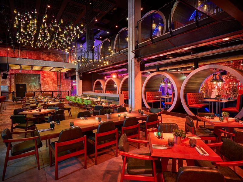 Gemütliche Bar mit Holz- und Lederstühlen, runden Nischen und warmen Lichterketten an der Decke.