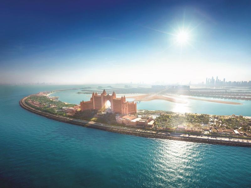 Insel mit Gebäuden und Stränden, umgeben von blauem Meer unter hellem Sonnenlicht.