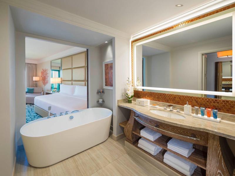 Moderner Badezimmerbereich mit freistehender Badewanne, großem beleuchtetem Spiegel und offenem Schlafzimmer.