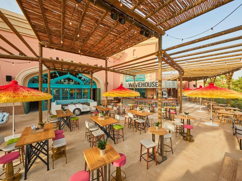 Großer, offener Gastraum mit Holzdecke, bunten Sonnenschirmen und vielen Holztischen und Stühlen.