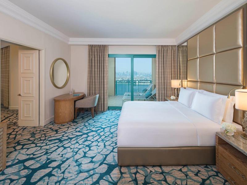 Modern eingerichtetes Hotelzimmer mit großem Bett, Schreibtisch, Teppich und Balkon mit Meerblick.