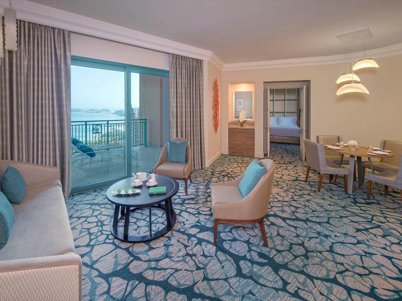 Helles Wohnzimmer mit Teppich, Sofas, Esstisch, Balkon und Meerblick bei Tageslicht.