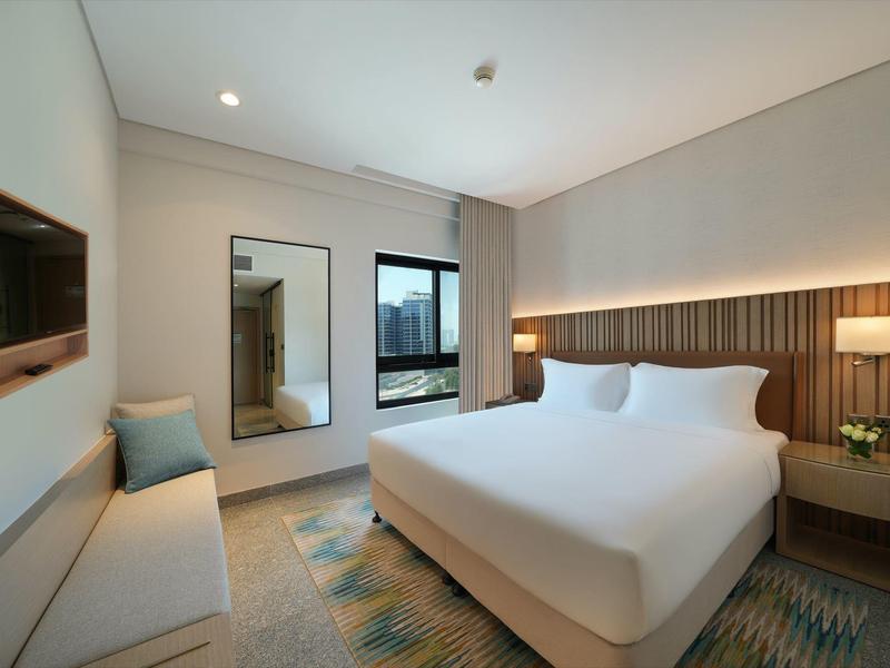 Modernes Schlafzimmer mit großem Bett, Holzpaneel, Spiegel, Sofa und Fenster mit Sicht nach draußen.