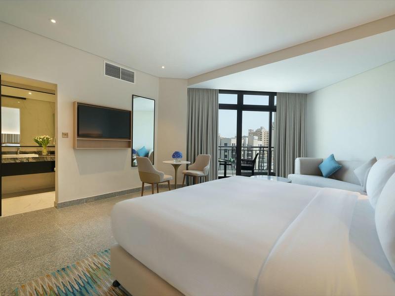 Geräumiges Hotelzimmer mit großem Bett, Schreibtisch, Fernseher und Balkon mit Stadtblick.