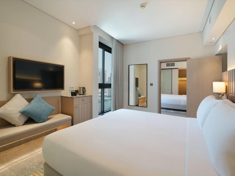 Modernes Schlafzimmer mit großem Bett, Wand-TV, Sofa, Spiegel und hellem, ruhigem Design.