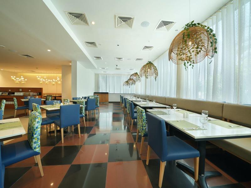 Modernes Restaurant mit blauen Stühlen, großen Fenstern und hängenden Pflanzgefäßen.