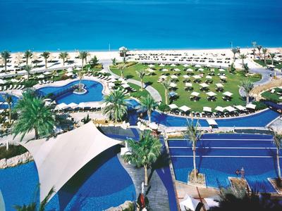 Große Poolanlage mit Liegen, Palmen und direktem Zugang zu einem blauen Sandstrand und Meer.