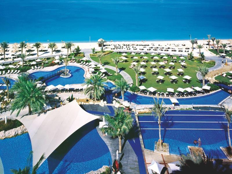 Große Poolanlage mit Liegen, Palmen und direktem Zugang zu einem blauen Sandstrand und Meer.