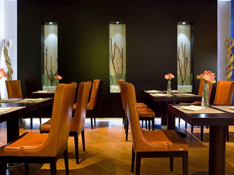 Modernes Restaurant mit braunen Ledersesseln, dunklen Wänden und dekorativen Leuchten an der Wand.