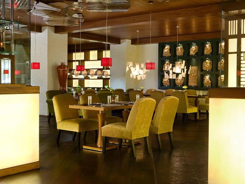 Modernes Restaurant mit warmen Holztönen, gelben Stühlen und dekorativen Wandmasken.