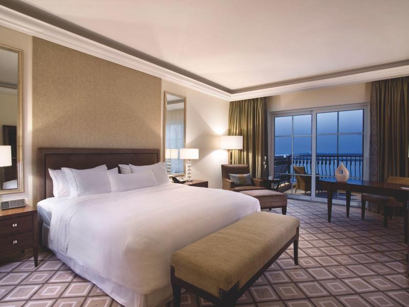 Modernes Hotelzimmer mit großem Doppelbett, Sitzbereich, Schreibtisch und Meerblick durch Fenster.