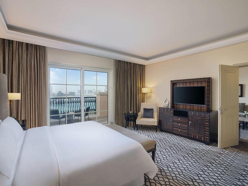 Geräumiges Hotelzimmer mit großem Bett, TV, Sessel, Balkon und Teppichboden in dezenten Farben.