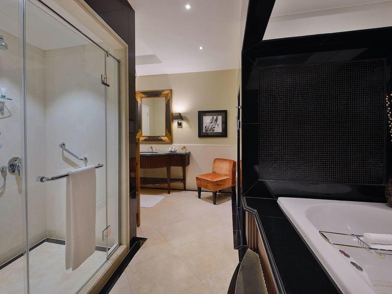 Badezimmer mit großer Dusche, dunkel gestrichener Wand und weißer Badewanne, helles angrenzendes Zimmer.