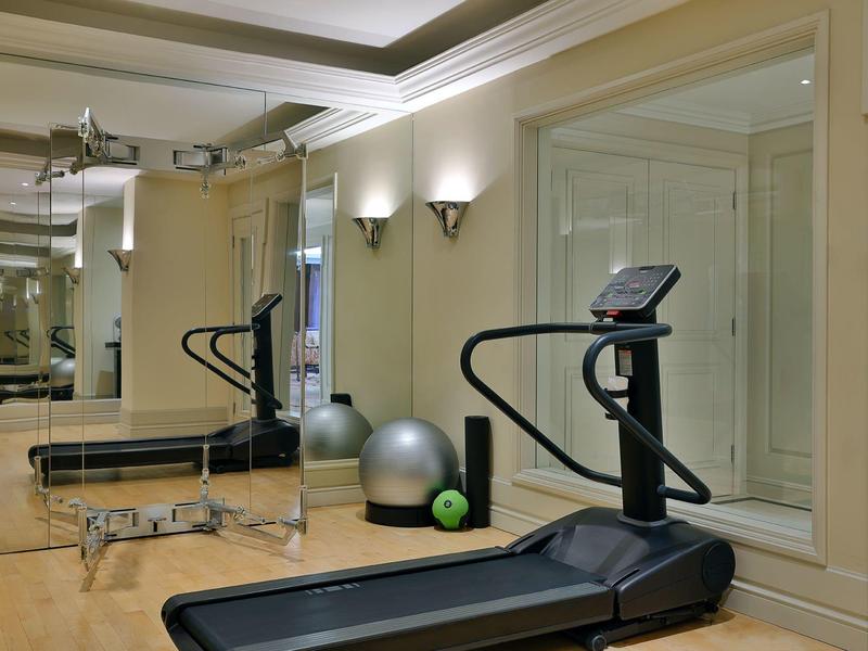 Ein heller Fitnessraum mit Laufband, Gymnastikbällen und Spiegelwänden auf hellem Holzboden.