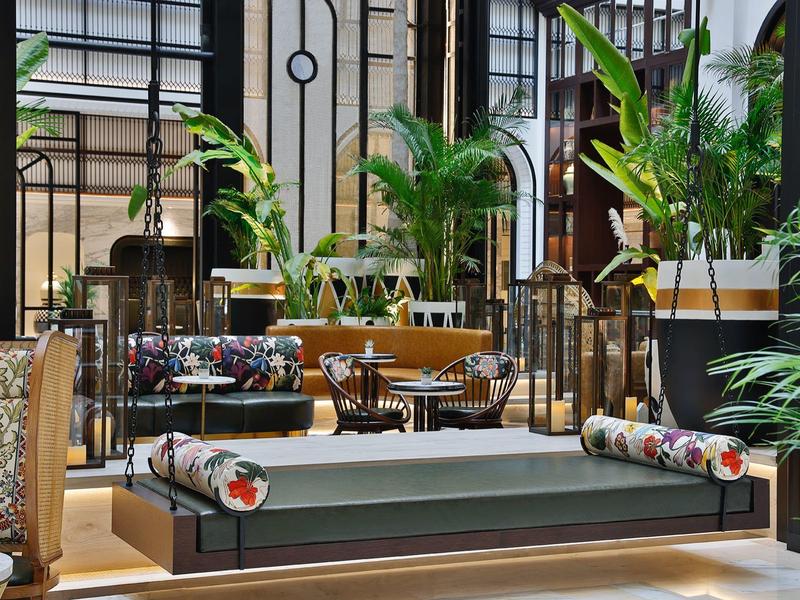 Moderner Loungebereich mit niedriger grauer Couch, bunten Kissen und grünen Pflanzen im Innenraum.