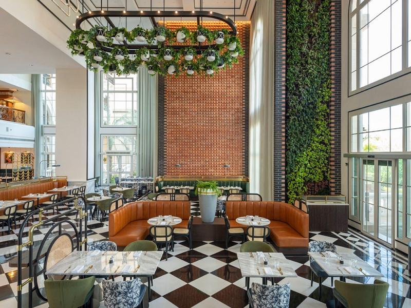 Modernes, helles Restaurant mit großen Fenstern, grünen Pflanzenwänden und elegantem Schwarz-Weiß-Boden.