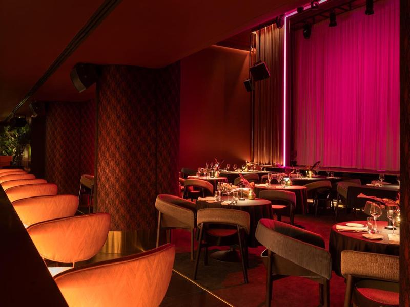 Gemütlicher, gedämpfter Veranstaltungsraum mit roten Vorhängen und elegant gedeckten Tischen.