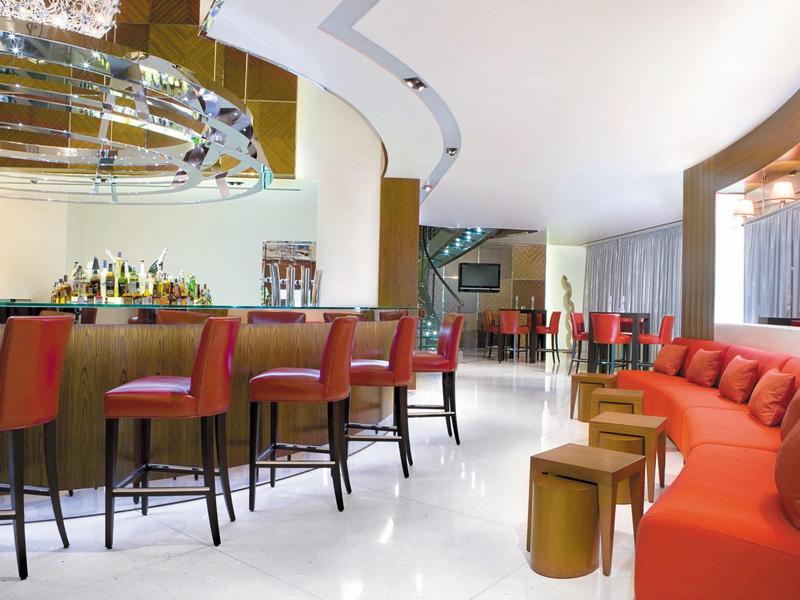 Moderner Barbereich mit roten Barhockern, runden Tischen und rotem Sofabereich, heller Boden.