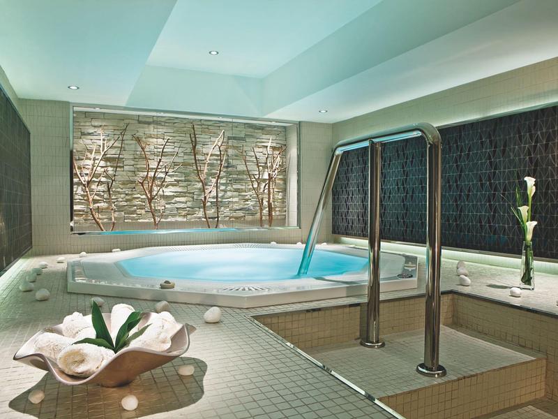 Moderner Wellnessraum mit Whirlpool, Mosaikfliesen, Metallgeländer und dekorativem Blumenarrangement.